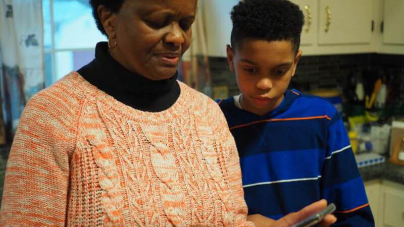 Thirteen-year-old Isaiah helps his grandmother, Carolyn Richardson, find a picture on her...